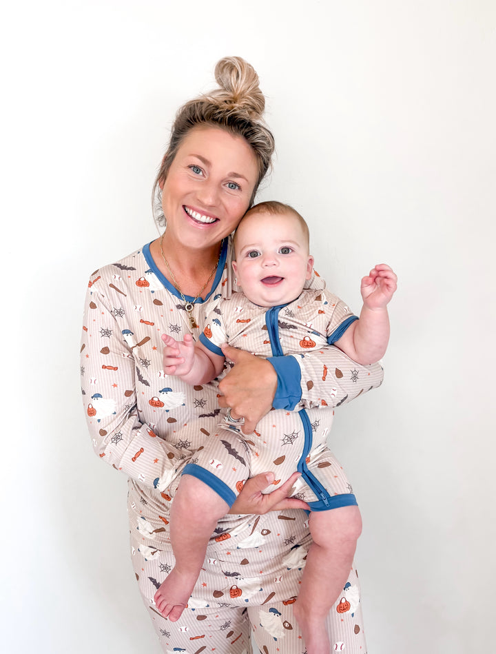 Woman and baby wearing matching tan fabric pajamas with a print of ghosts, baseballs, bats, and pumpkins.