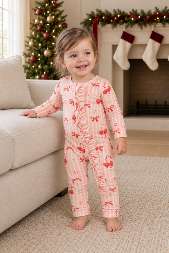 Toddler beside an ivory sofa wearing pink striped Peppermint Lane ruffle convertible zip footies.
